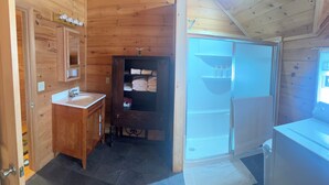 A wooden cabin bathroom with a sink, mirror, towel rack, and a shower area.