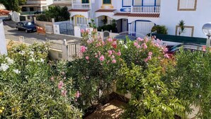 Un quartier résidentiel avec des maisons blanches, des balcons et un jardin où poussent des fleurs roses.