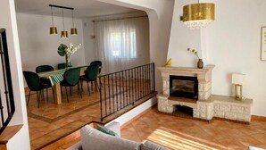 Un salon avec une cheminée, un coin repas avec des chaises vertes et un escalier.
