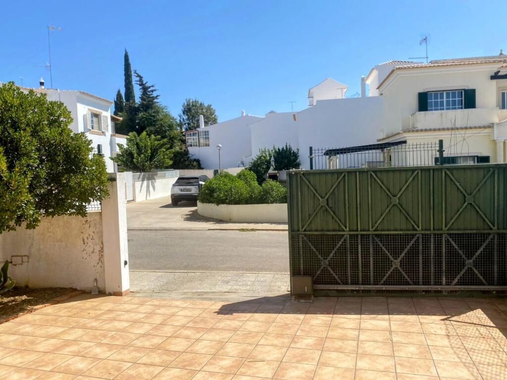 Une rue résidentielle bordée de maisons, avec une entrée sécurisée et un ciel dégagé.