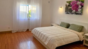 Une chambre à coucher avec un lit, une fenêtre avec des rideaux, une table de chevet et une lampe fixée au mur.