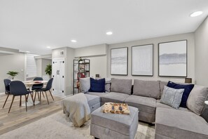 A modern living room with a grey sectional sofa, a dining table with chairs, and a coffee table with a tray. - 5BR Toledo Retreat, Hot Tub, Sauna, Sleeps 14 (Toledo)