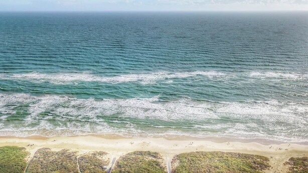 An aerial view of a beach with waves, sandy shore, and sparse vegetation. - Beautiful 4Ba/Br, oceanfront, & ground floor- one of only several on the island! (South Padre Island)