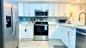 A modern kitchen with stainless steel appliances, white cabinetry, and a tiled backsplash. - Beautiful 4Ba/Br, oceanfront, & ground floor- one of only several on the island! (South Padre Island)