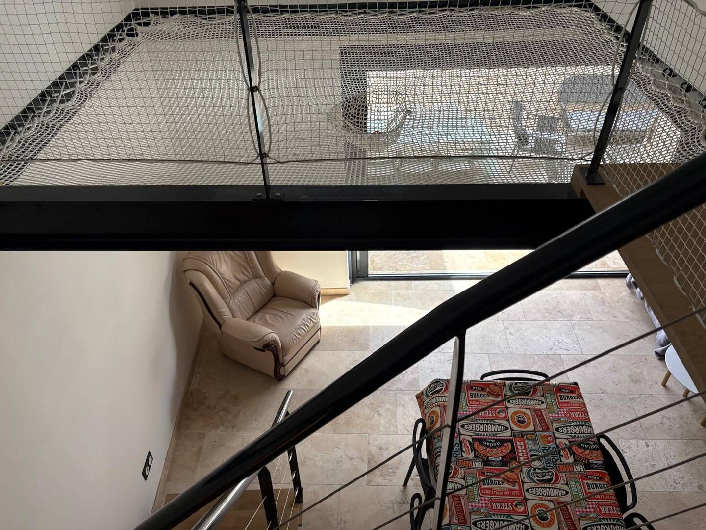 A room with a high ceiling, a chair, a table with a patterned tablecloth, and a view through a window.