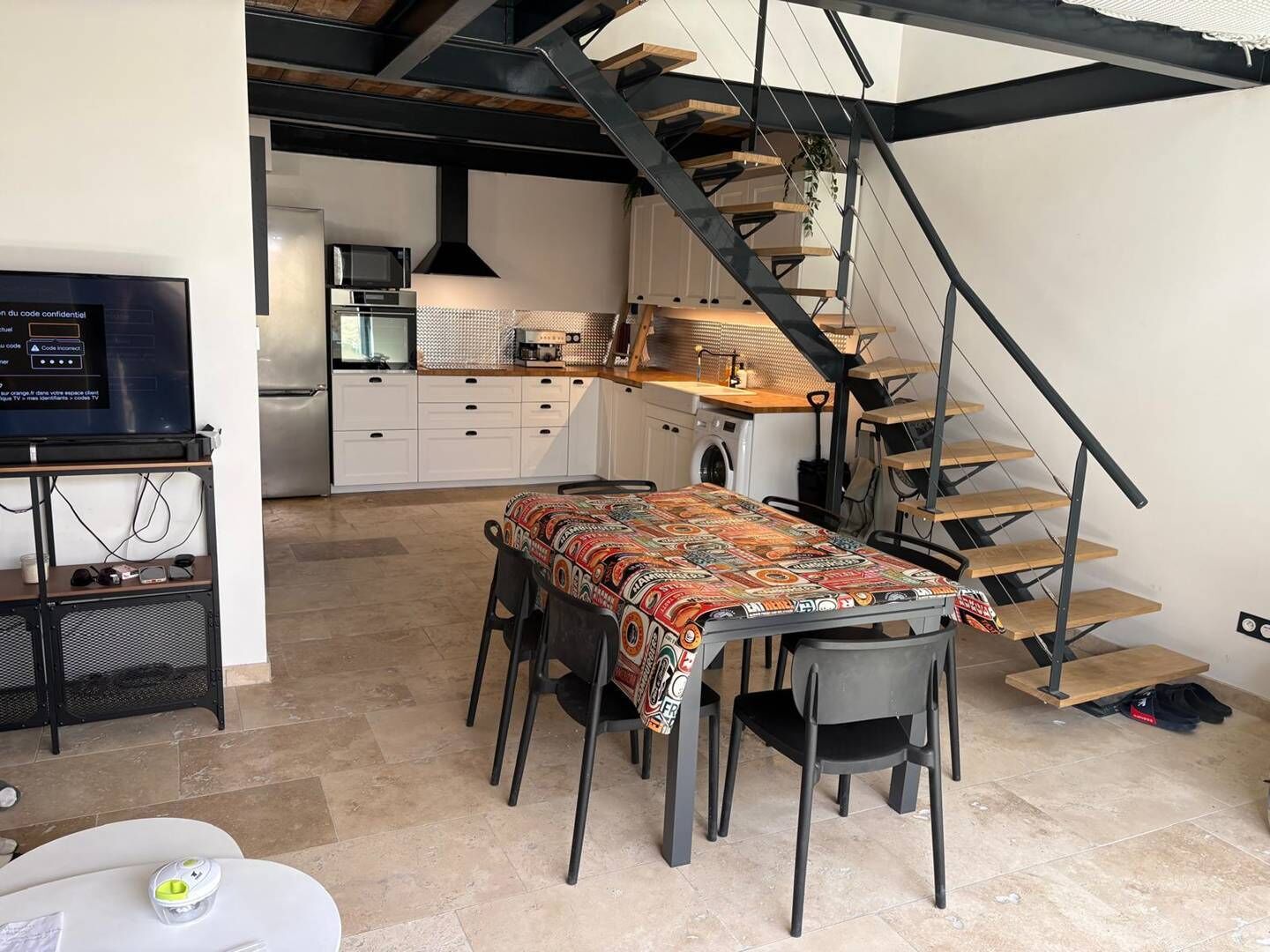 Une cuisine moderne équipée d’un four, d’un micro-ondes et d’un évier intégrés. On y trouve également un coin repas avec une table et des chaises, ainsi qu’un escalier menant à l’étage supérieur.