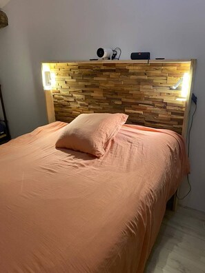 A bedroom with a wooden headboard, a bed with peach bedding, and a bedside table with a lamp. - AUTHENTIC WINEGROWER'S HOUSE 10 MIN FROM THE BEACHES (FLEURY)
