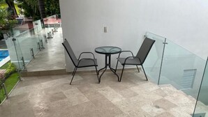 Ein Balkon mit Glasgeländer, einem runden Tisch und zwei Stühlen.