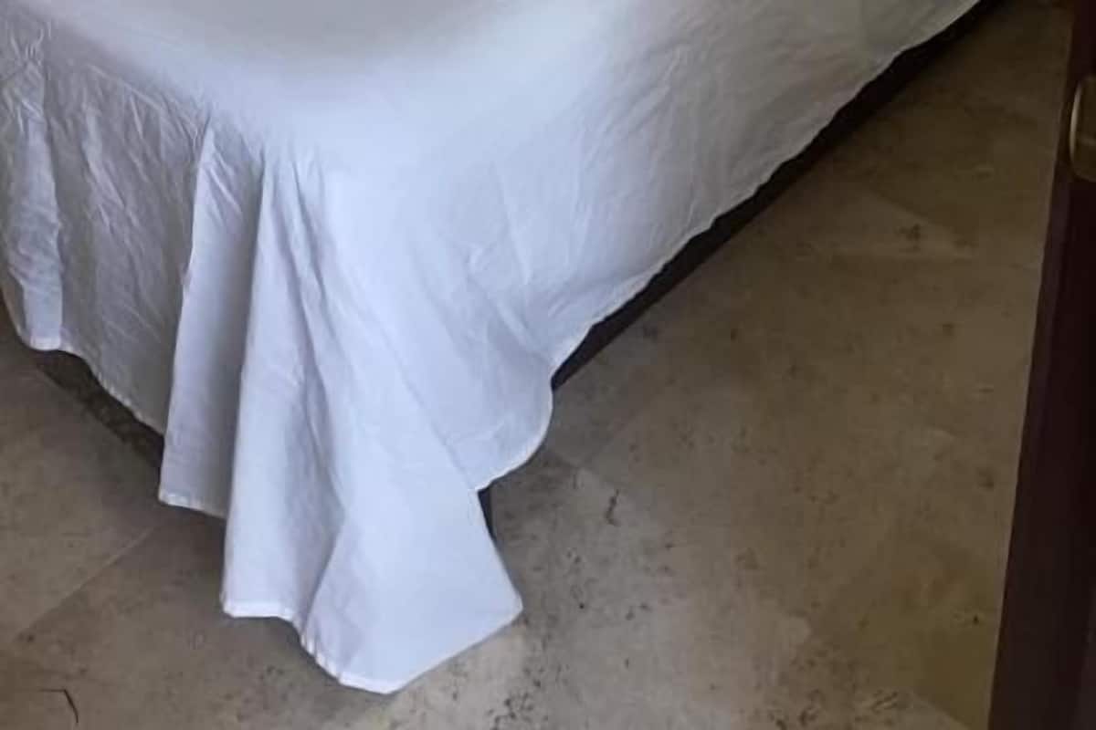 A single bed with white bedding, a nightstand, and a wall socket.