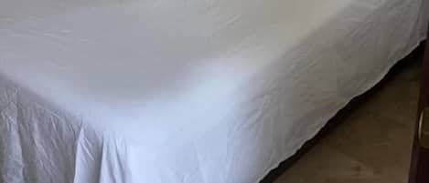 A single bed with white bedding, a nightstand, and a wall socket.