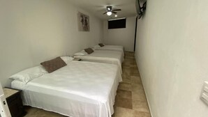 Ein Zimmer mit zwei Betten, einem Deckenventilator, einem Wandfernseher und einem kleinen Fenster.