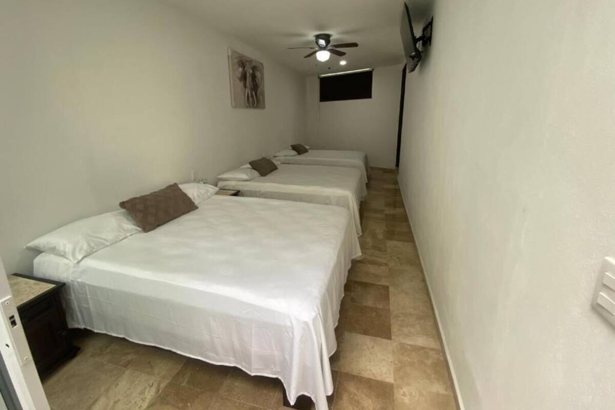 A room with two beds, a ceiling fan, a mounted TV, and a small window.