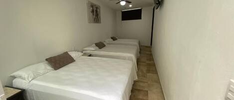 A room with two beds, a ceiling fan, a mounted TV, and a small window.