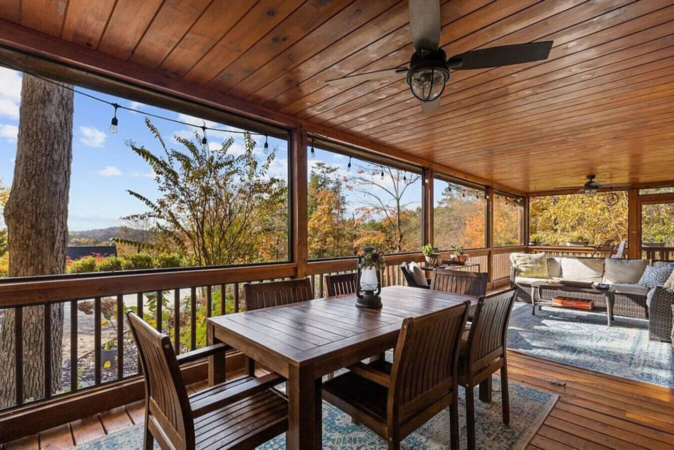 A covered outdoor area with a wooden table and chairs, a sofa, and a ceiling fan.