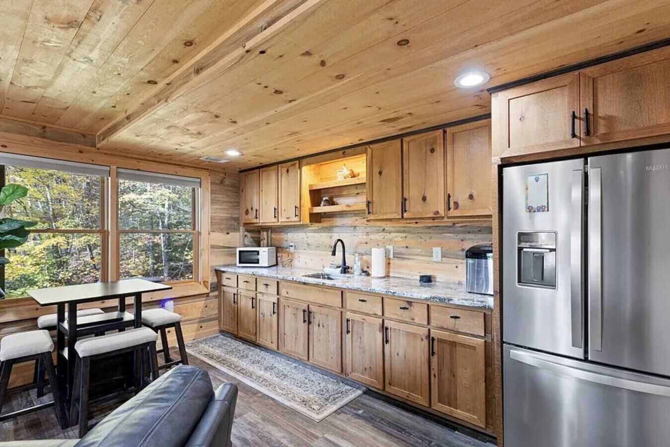 A wooden cabin interior with a kitchen, dining area, and a large window.
