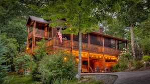 A two-story log cabin with a balcony, surrounded by lush greenery. - Luxury Mountain House|HotTub|Decks|Shuffleboard (Mineral Bluff)