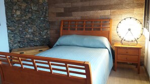 Ein Schlafzimmer mit einem hölzernen Bett, einer Steinwand und einem Nachttisch mit einer Lampe.