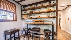 Une cuisine avec un mur en briques, des étagères en bois et trois tabourets.