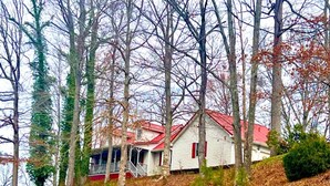Une maison avec un toit rouge, entourée d’arbres et située au pied d’une colline.