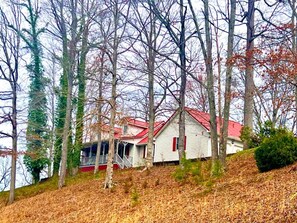 A house with a red roof, surrounded by trees and a hill.