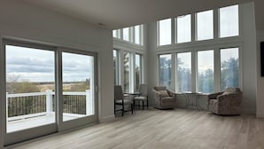 Une pièce spacieuse dotée de grandes fenêtres, d’un balcon et d’un coin salon avec deux fauteuils et une table.