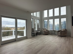 A spacious room with large windows, a balcony, and a seating area with two chairs and a table. - new large home w/swimming pool, ocean views plenty of parking incredible sunsets (Cape May)
