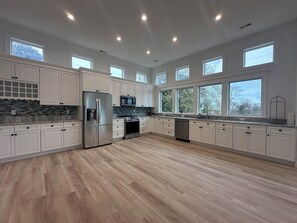 A spacious kitchen with white cabinets, stainless steel appliances, and large windows. - new large home w/swimming pool, ocean views plenty of parking incredible sunsets (Cape May)