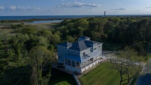 Une maison à deux étages dotée d’un balcon, entourée d’une végétation luxuriante et offrant une vue sur l’océan.