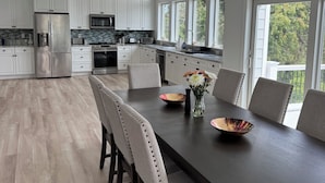 Une cuisine moderne avec des meubles blancs, un réfrigérateur en acier inoxydable et un coin repas comprenant une table et des chaises en bois foncé.