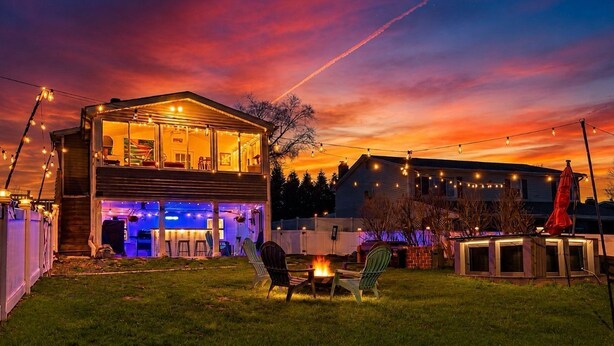 A two-story house with a deck, outdoor seating, and string lights.