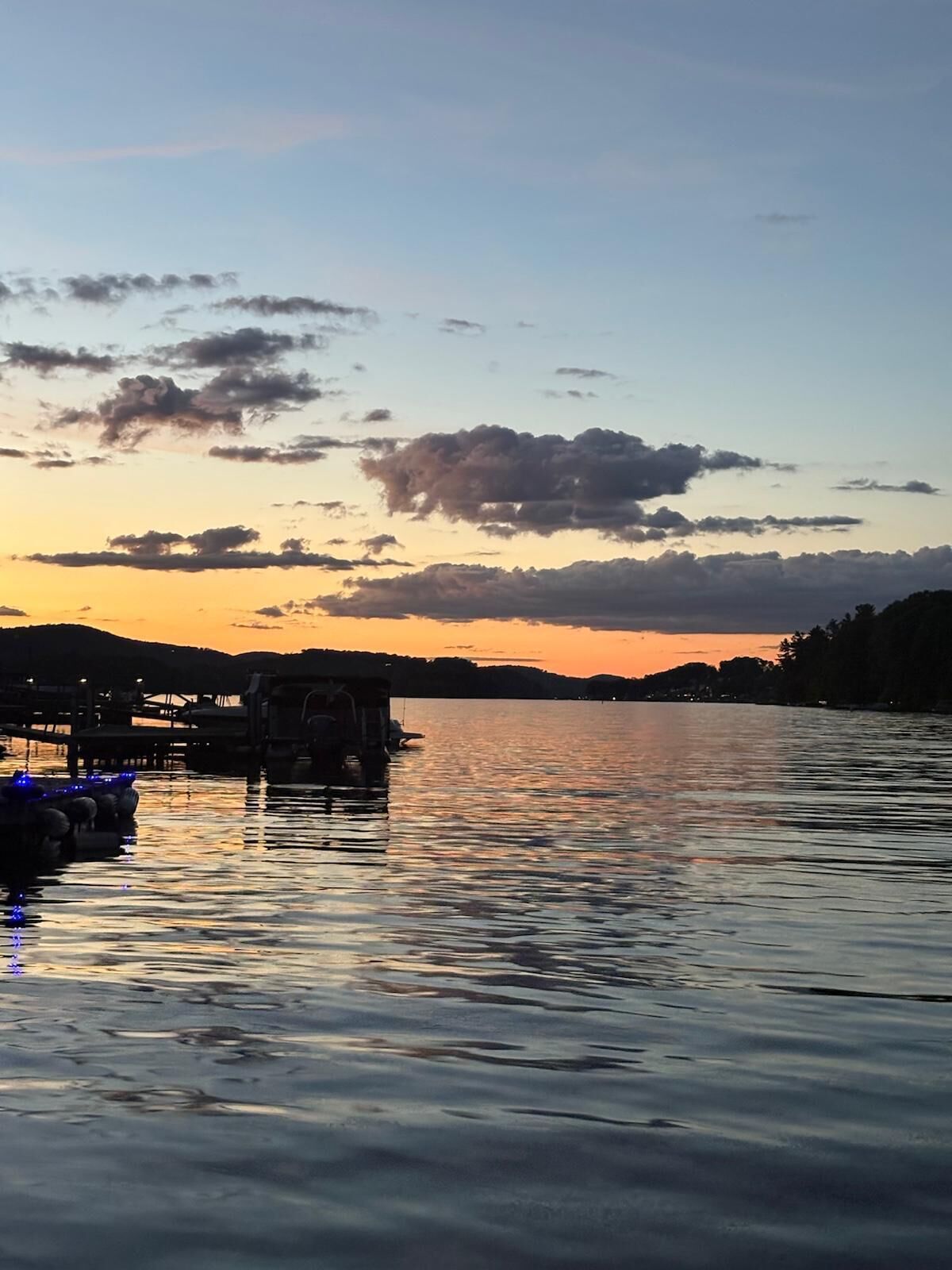 Un lac paisible au coucher du soleil, avec des bateaux amarrés sur la rive gauche.