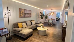 A modern living room with a sofa, a coffee table, and a dining area in the background.