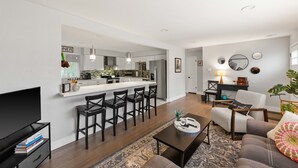 A modern living room with a TV, books, a coffee table, and a sofa. - Modern 4BR Retreat: Private Yard - 10 Min to DEN (Arvada)