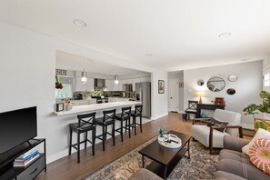 A modern living room with a TV, books, a coffee table, and a sofa. - Modern 4BR Retreat: Private Yard - 10 Min to DEN (Arvada)