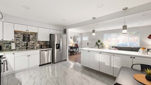 A modern kitchen with white cabinetry, a stainless steel refrigerator, and a marble floor. - Modern 4BR Retreat: Private Yard - 10 Min to DEN (Arvada)
