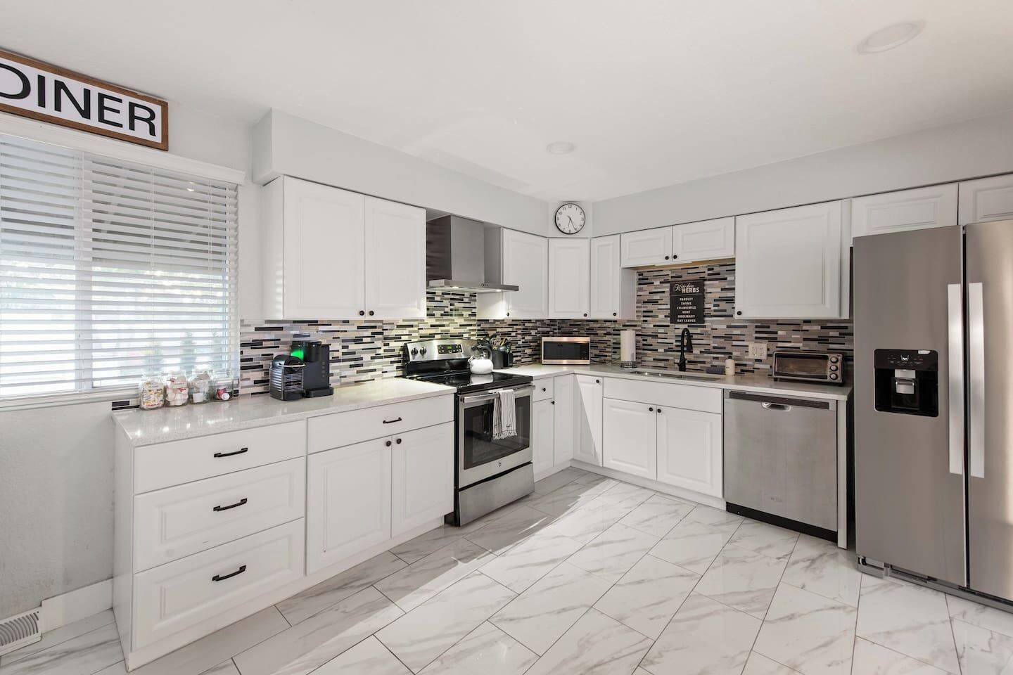 A modern kitchen with white cabinetry, a stainless steel refrigerator, a microwave, and a coffee maker.
