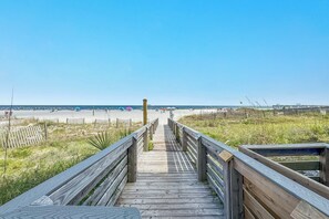 Ein hölzerner Steg führt zu einem Strand unter blauem Himmel.