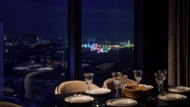 Ein Esstisch, gedeckt mit Geschirr, mit Blick auf die Stadt durch große Fenster.