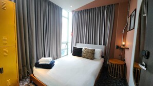 Habitación de hotel con cama, cortinas, mesita de noche, lámpara y armario.