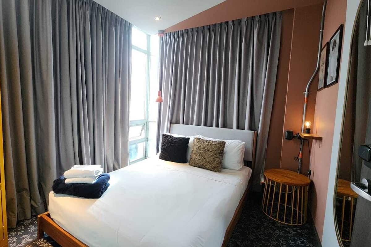 A hotel room with a bed, curtains, a bedside table, a lamp, and a wardrobe.