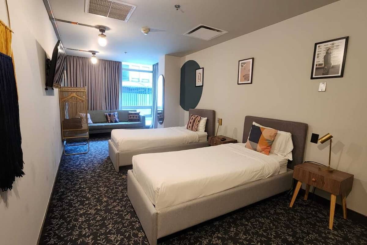 A hotel room with two beds, a sofa, a TV, and a window with curtains.