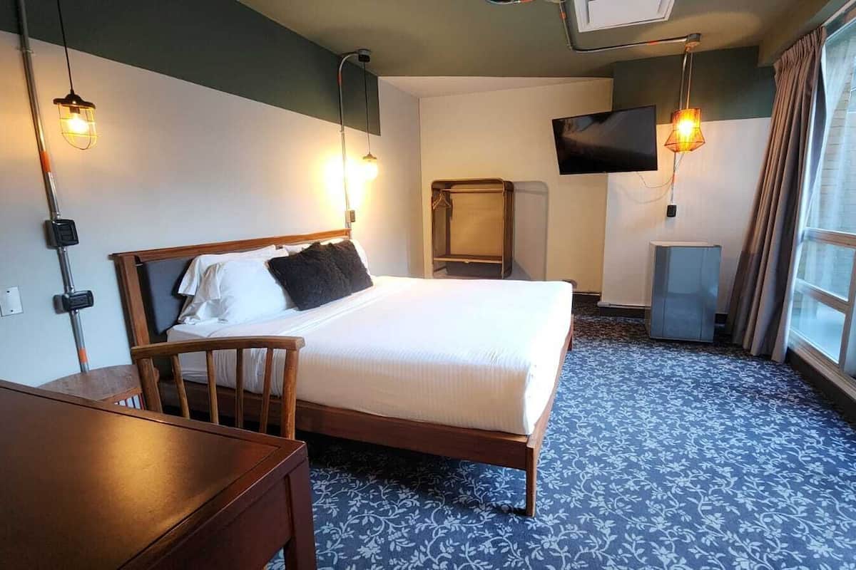 A hotel room with a bed, a desk, a chair, a television, and a window.