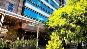 Un edificio moderno con fachada de vidrio, zona de estar al aire libre y vegetación.