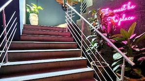 Una escalera con barandales de metal, plantas en macetas y un letrero de neón.