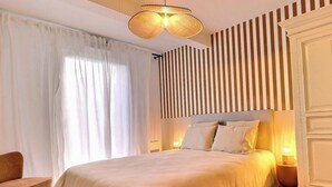 A bedroom with a bed, a chair, a bedside table, and a wall-mounted light fixture. - Les Elfes - DINARD - City break (DINARD)