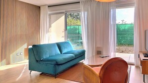 A modern living room with a blue sofa, a wooden floor, a round table, and a TV. - Les Elfes - DINARD - City break (DINARD)
