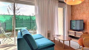 A modern living room with a sofa, a TV, a small table, and a sliding glass door leading to an outdoor area. - Les Elfes - DINARD - City break (DINARD)
