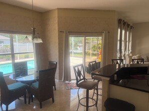 A dining area with a pool view, wicker chairs, a bar, and a large window. - 3-bedroom heated Pool house in beautiful Palm Coast/Flagler Beach (Palm Coast)