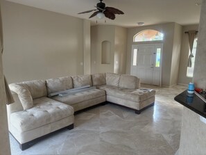 A living room with a sectional sofa, a ceiling fan, a door with a window, and a tiled floor. - 3-bedroom heated Pool house in beautiful Palm Coast/Flagler Beach (Palm Coast)