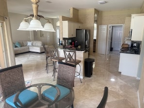 A spacious living area with a glass-top dining table, wicker chairs, a sofa, and a kitchen with a refrigerator and microwave. - 3-bedroom heated Pool house in beautiful Palm Coast/Flagler Beach (Palm Coast)